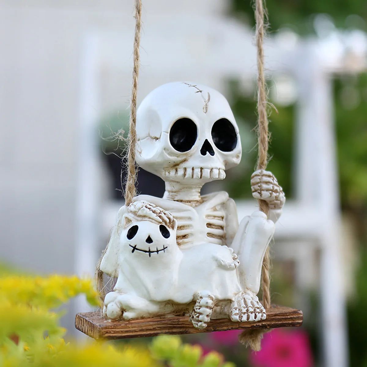 A white skull and skeleton ghost figurine hanging by twine against a blurred outdoor background.