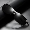 A pair of black photochromic polarized driving sunglasses with an alloy frame resting on a dark surface.
