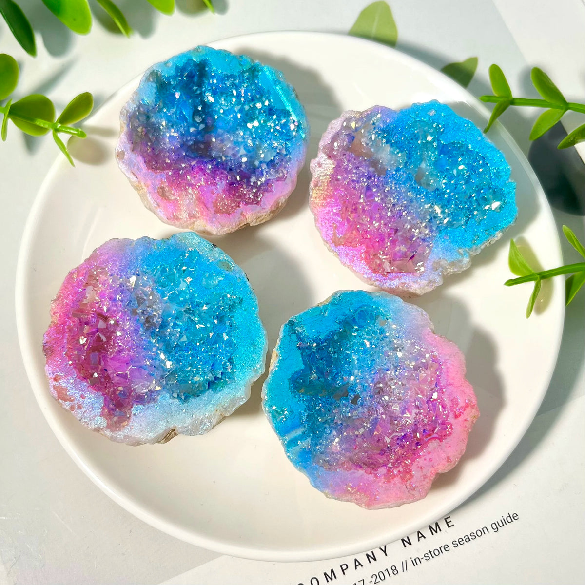 Four iridescent blue and pink crystal geode slices arranged on a white plate.