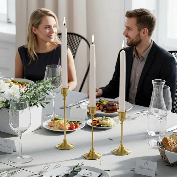 Three tall gold vintage metal candle holders with white candles on a white table for elegant decor