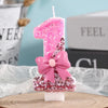 A pink glitter birthday candle shaped like the number one with a bow on a wooden surface.