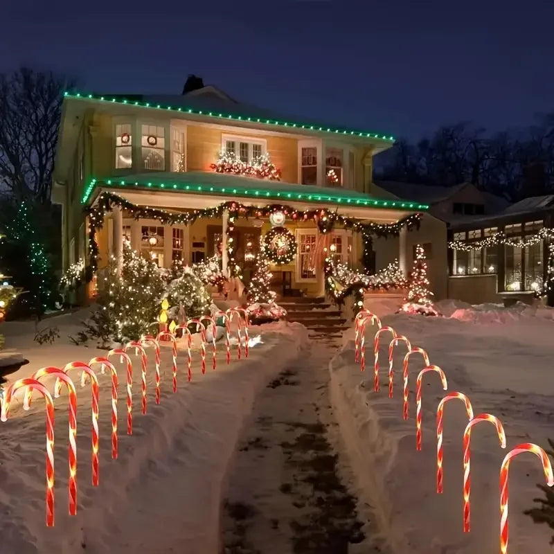 A pathway lined with red and white candy cane lights illuminates a house decorated for Christmas at night.