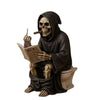 A dark resin statue of a skull wearing a hooded cloak and holding a newspaper, depicting a middle finger gesture.