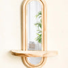 A wooden arched mirror with a natural wood shelf mounted on a light wall.