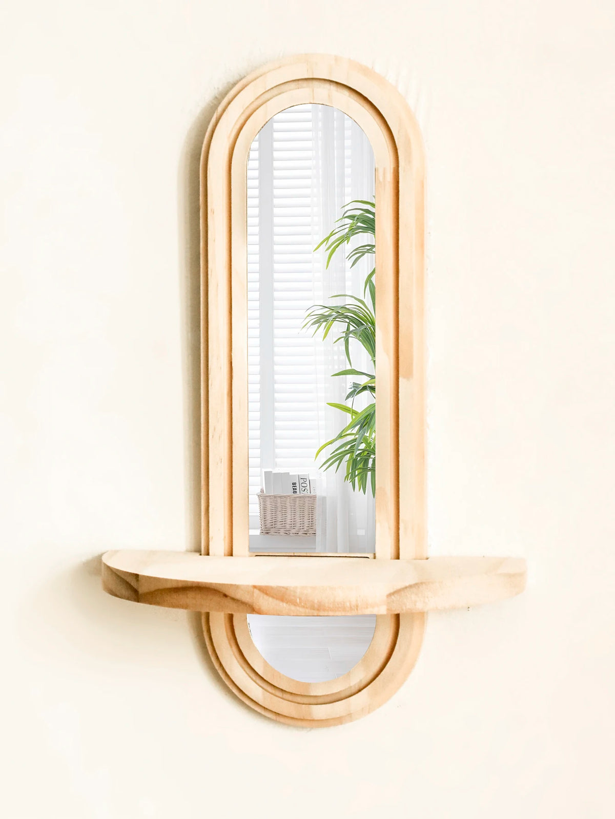 A wooden arched mirror with a natural wood shelf mounted on a light wall.
