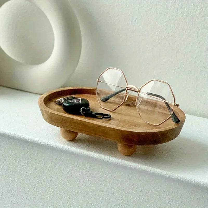 A pair of clear-framed glasses rests on a wooden tray next to a black clip.