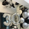 A cluster of metallic silver foil balloons shaped like the numbers 3 and 0, displayed indoors.