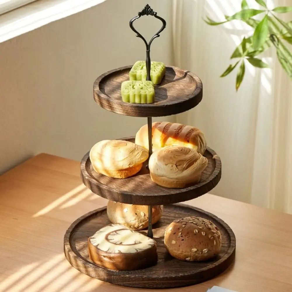 A wooden 3-tier cupcake stand displaying various baked goods like bread rolls and cupcakes.