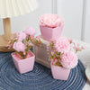 A set of three pink artificial rose potted plants displayed on a blue textured surface.