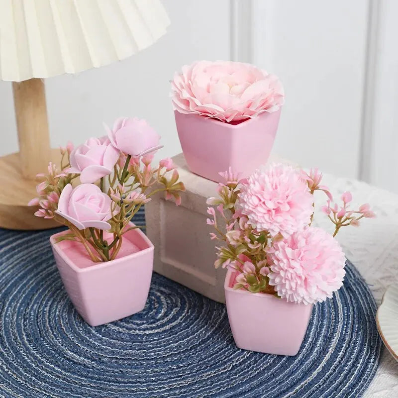 A set of three pink artificial rose potted plants displayed on a blue textured surface.