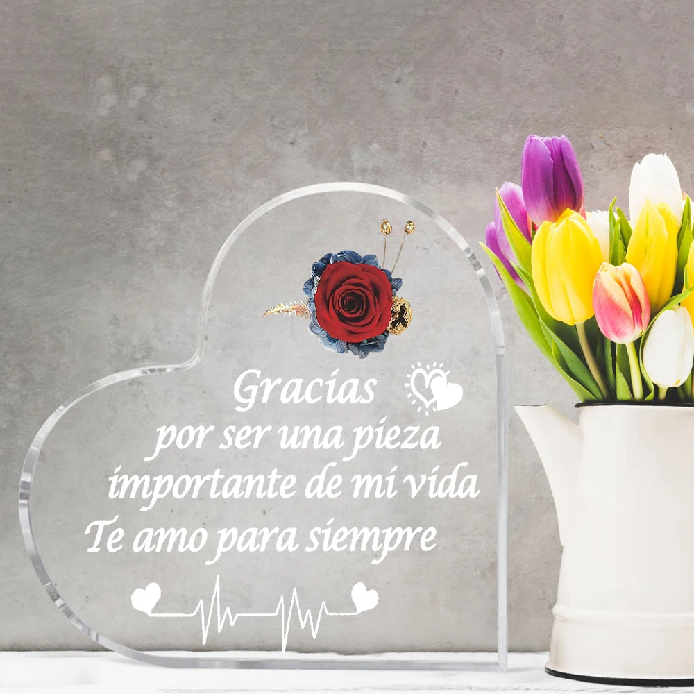 A clear heart-shaped glass frame engraved with the Spanish phrase Gracias por ser una pieza importante de mi vida Te amo para