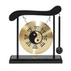 A black desktop zen gong with a circular brass plate and wooden mallet hanging from a curved wooden stand.