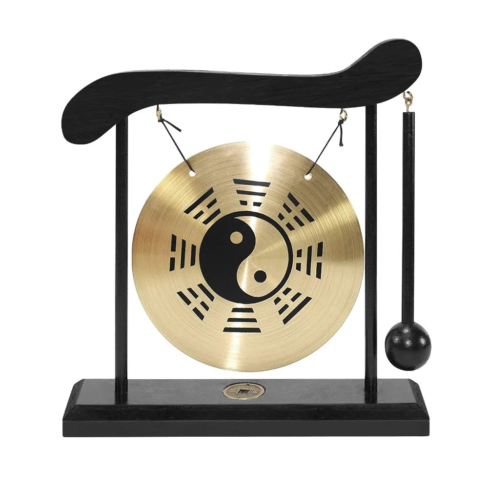 A black desktop zen gong with a circular brass plate and wooden mallet hanging from a curved wooden stand.