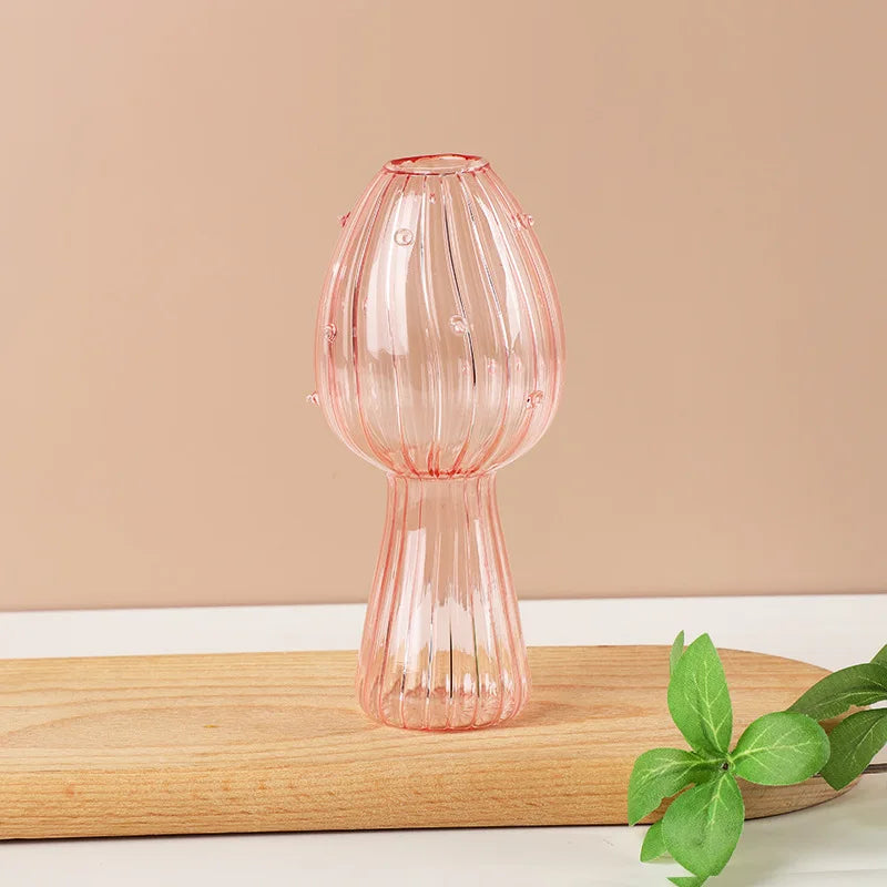 A pink, translucent glass vase shaped like a mushroom, resting on a light wooden surface.