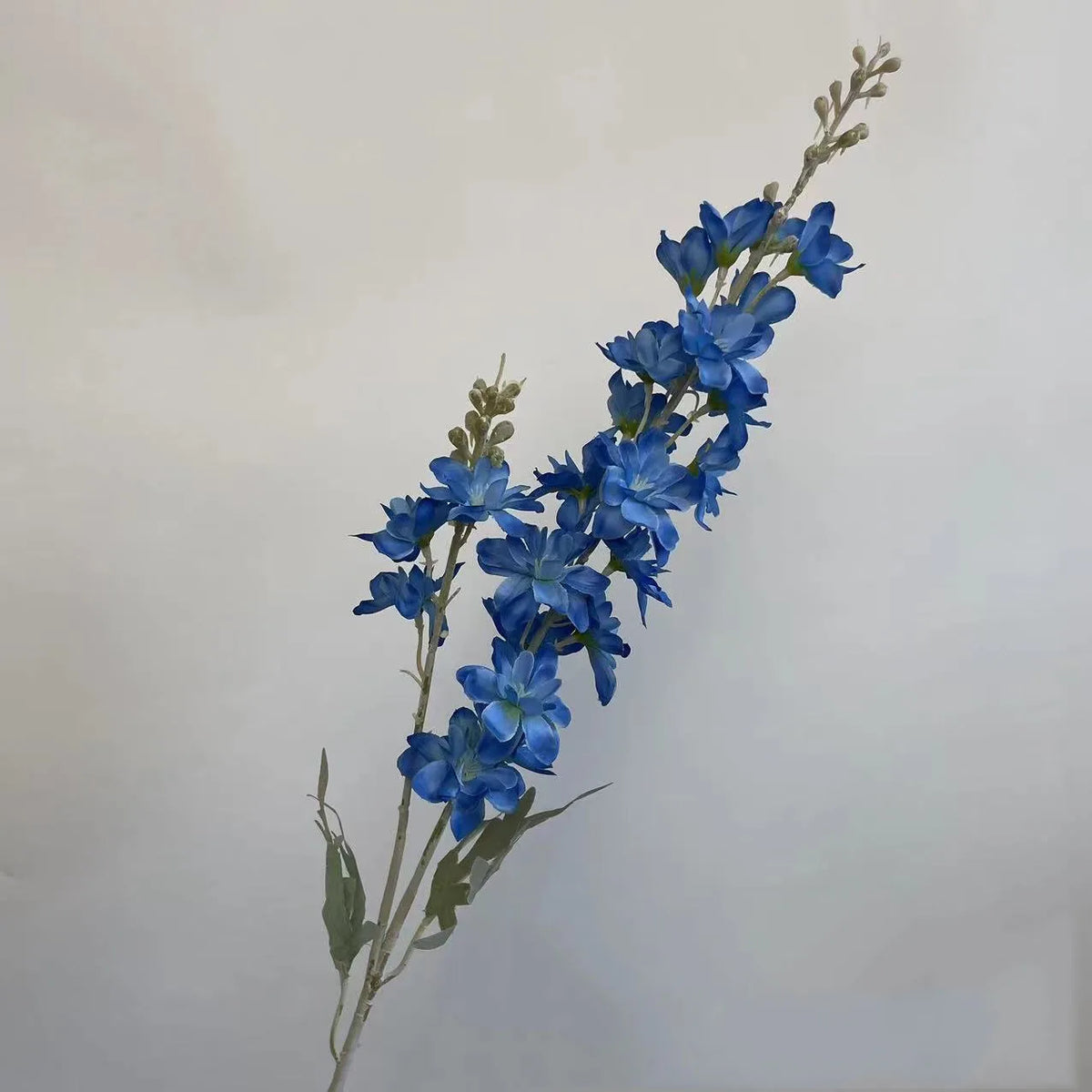 Une tige mince de fleurs de delphinium artificielles bleues avec de petites feuilles et bourgeons.