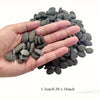 A hand holds a pile of smooth, dark gray river rocks ranging in size from 1-3cm to 0.39-1.18 inches.