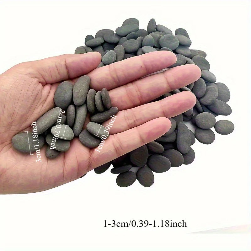 A hand holds a pile of smooth, dark gray river rocks ranging in size from 1-3cm to 0.39-1.18 inches.