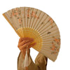 A hand holds an elegant bamboo folding fan with a light beige background and pink floral bird print.