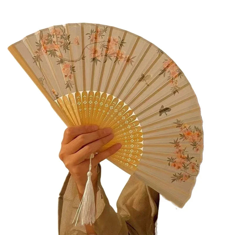 A hand holds an elegant bamboo folding fan with a light beige background and pink floral bird print.