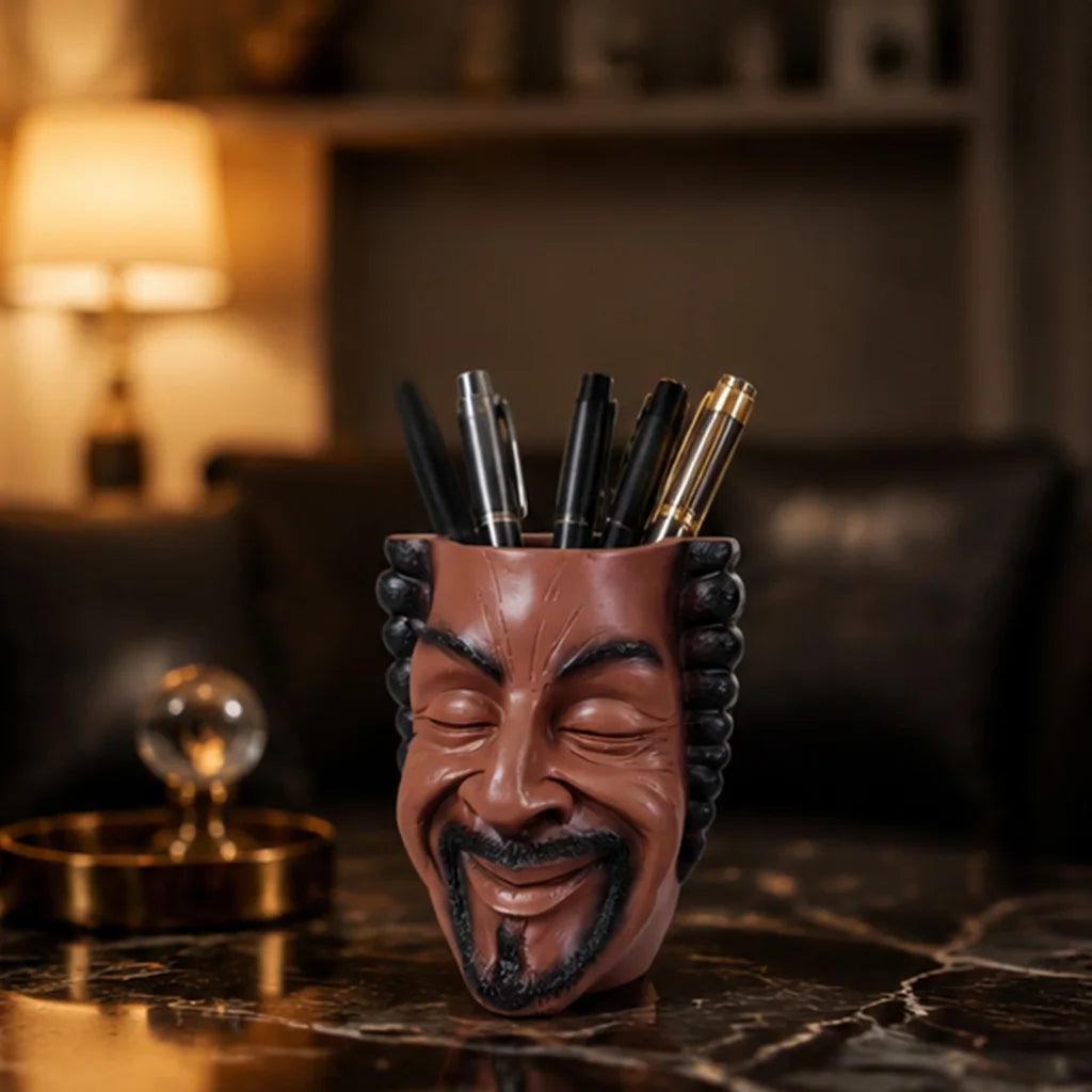 A terracotta-colored artistic face planter holds several black pens on a dark marble surface.