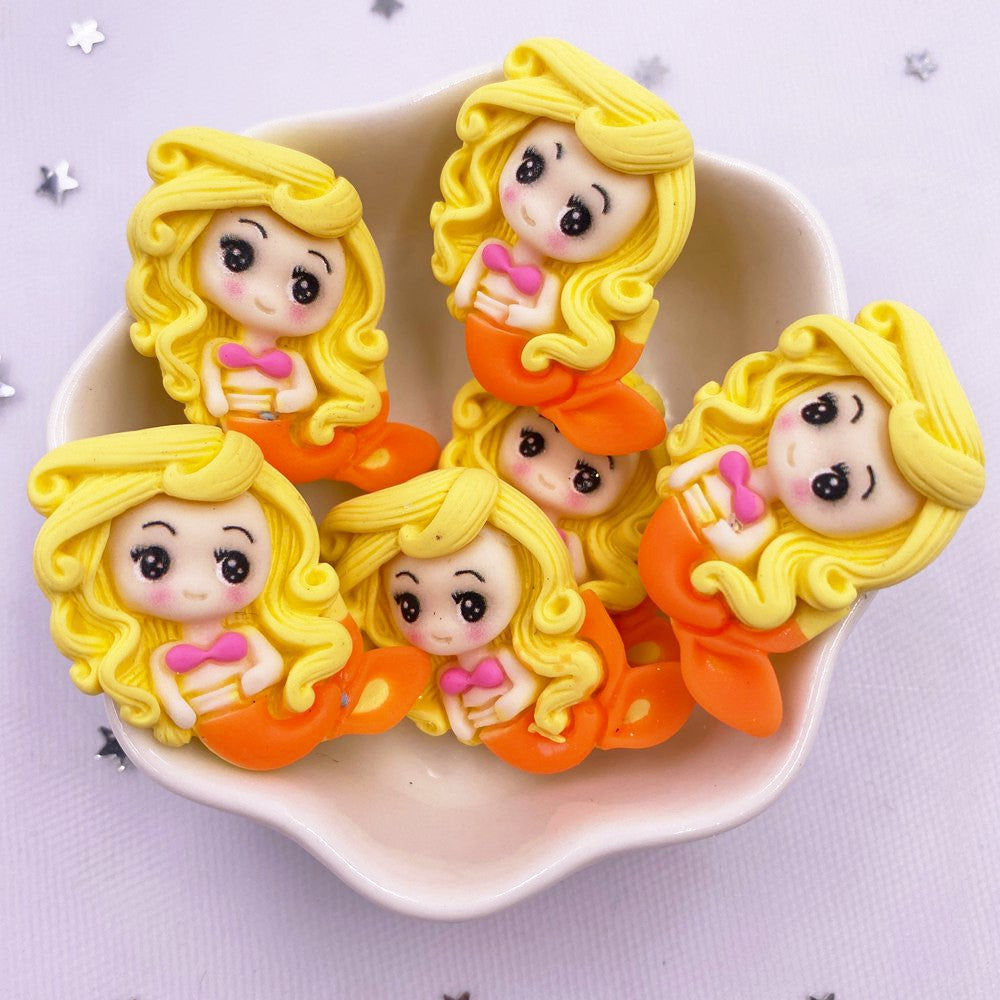 A collection of yellow mermaid princess resin figurines with pink accents arranged on a white dish.