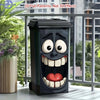 Poubelle noire décorée d'un visage de dessin animé amusant avec la bouche ouverte et les dents.