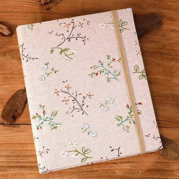 A beige linen photo album with delicate green and pink floral embroidery rests on a wooden surface.