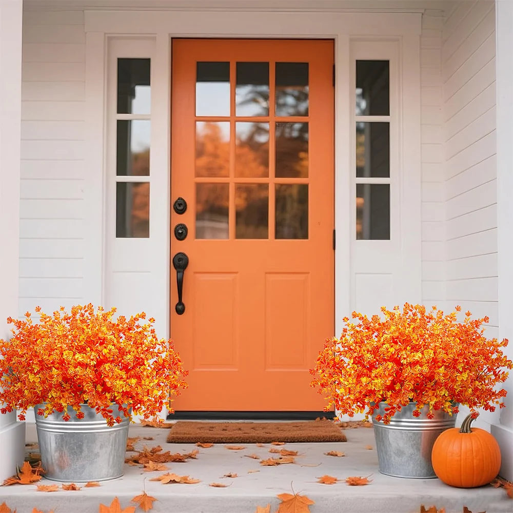 An orange door with glass panels is set in a white frame, flanked by vertical windows. Autumn leaves and orange foliage decor
