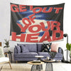 A dark tapestry wall hanging with red text that reads Get Out of Your Head displayed above a modern sofa.