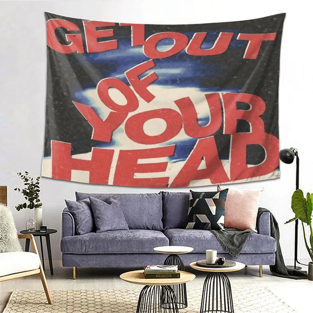 A dark tapestry wall hanging with red text that reads Get Out of Your Head displayed above a modern sofa.