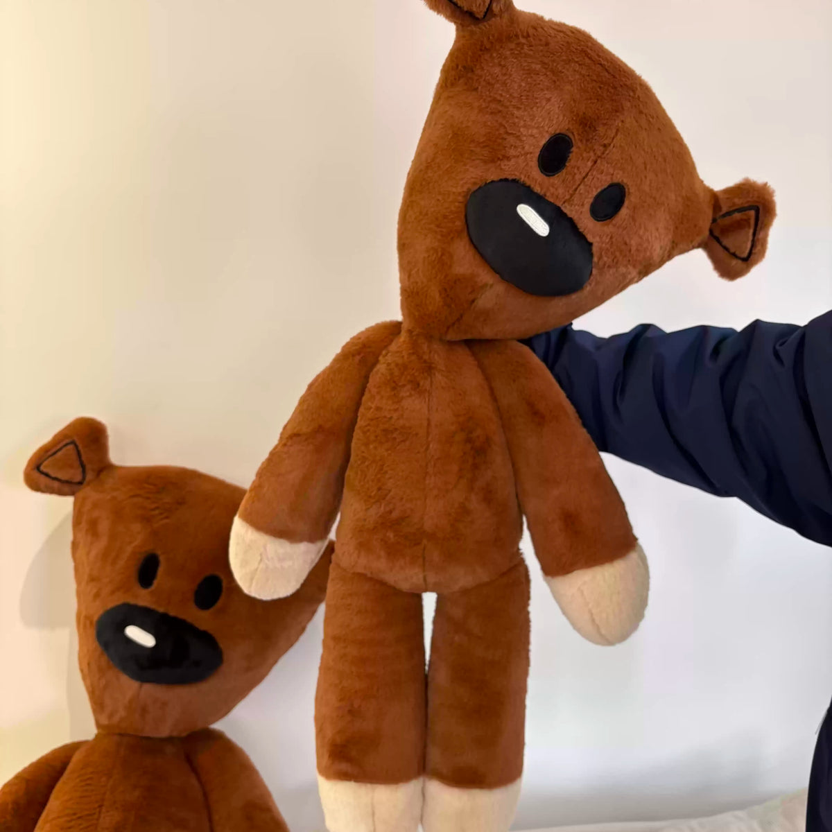 A brown teddy bear stuffed plush toy is shown next to a person's hand.