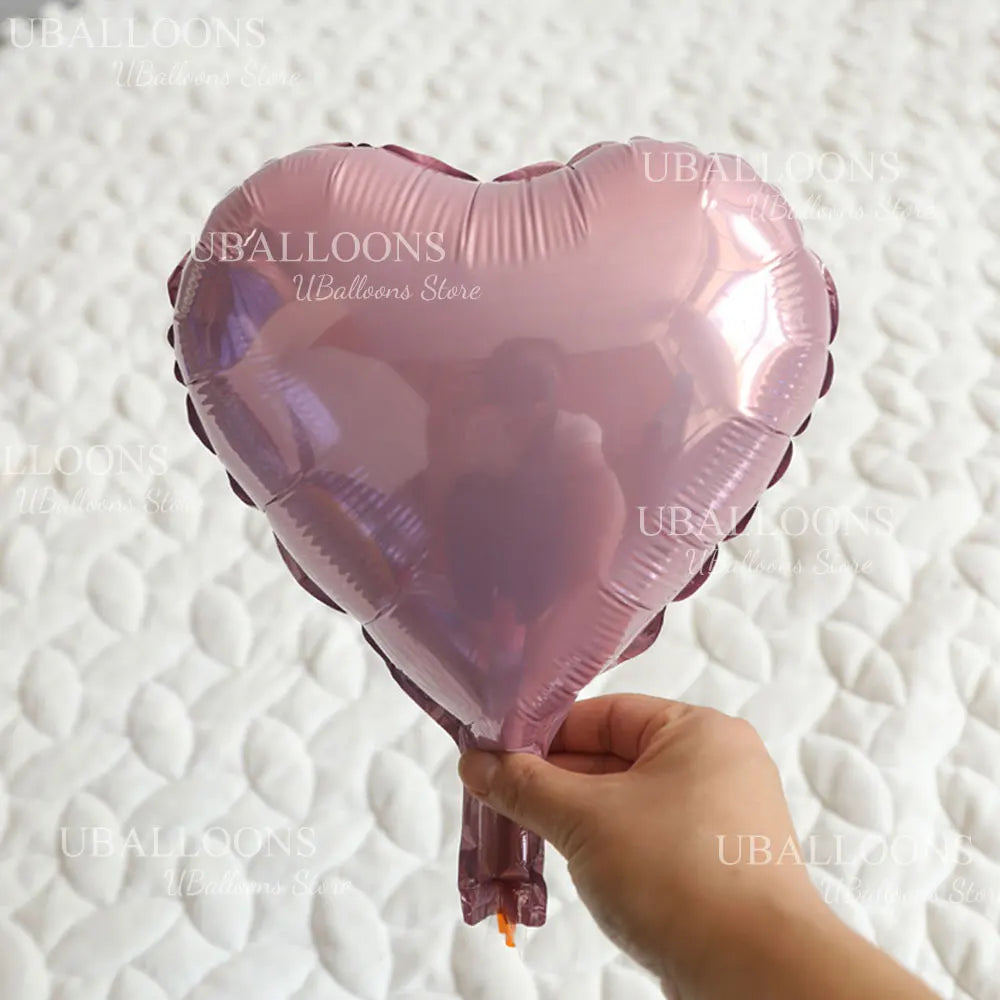 A pink heart-shaped foil balloon is being held by a person against a white textured background.