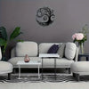 A modern living room featuring a light gray sofa, white coffee table, and a black tree of life metal wall art above it.