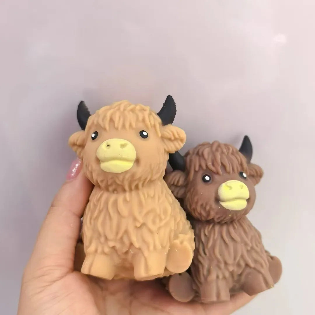 A hand holds a brown Scottish Highland cow squishy stress relief toy.
