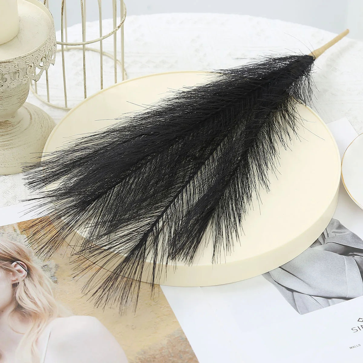 A black artificial pampas grass bouquet displayed on a light cream plate.