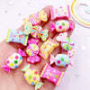 A hand holds various colorful candy resin cabochons in pink and purple hues for crafting projects.