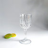 A clear glass wine glass with a diamond pattern sits on a white surface next to two lime slices.