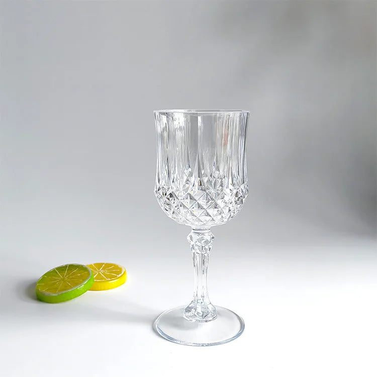 A clear glass wine glass with a diamond pattern sits on a white surface next to two lime slices.