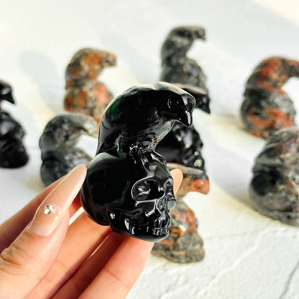Une main tient un crâne de corbeau en obsidienne polie, décor entouré de sculptures en pierre sombre.