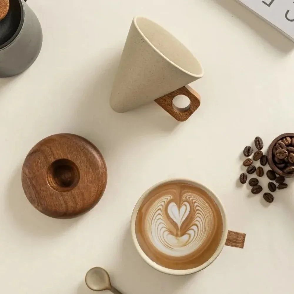 A ceramic coffee mug with a light beige conical lid rests on a wooden coaster next to a latte art cup.