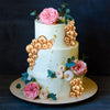 A two-tiered white cake decorated with pink roses and gold spherical accents on a dark background.