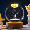 A glowing crystal ball night light featuring a deer silhouette on a dark background, resting on a wooden base.