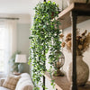 Artificial eucalyptus hanging plant with green leaves cascading down, displayed on a wooden shelf.