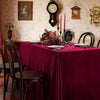A long table set for dining with a burgundy red velvet tablecloth, dark wooden chairs, and decorative items.