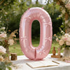 A large pink foil number balloon shaped like zero resting on a white table surrounded by floral greenery.