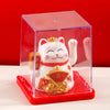 A white and gold solar-powered waving lucky cat figurine displayed inside a clear red box.