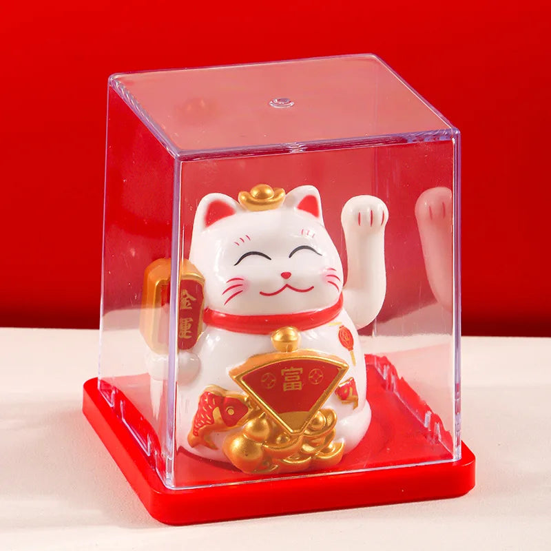 A white and gold solar-powered waving lucky cat figurine displayed inside a clear red box.