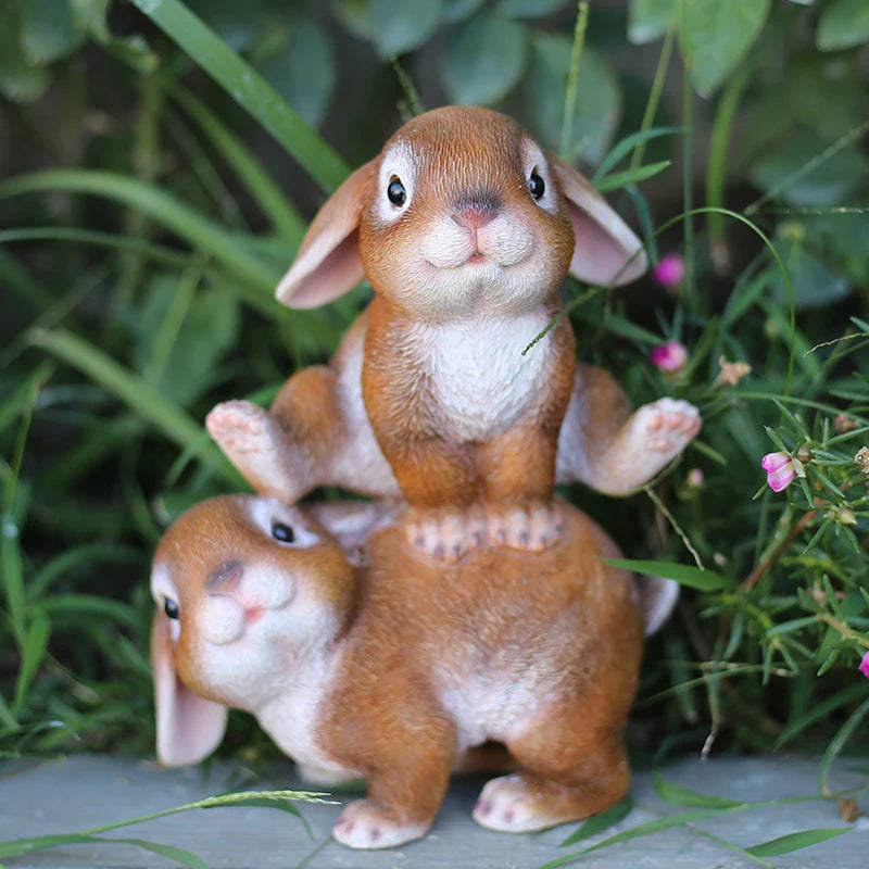 A hand-painted resin rabbit garden statue with brown and white fur sitting in green foliage.