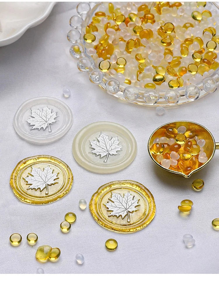 A collection of transparent wax sealing beads in yellow and amber tones, displayed in a glass bowl and on white discs.