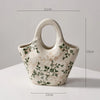A white ceramic milk pitcher with a handle and pastoral floral design, shown from the side.